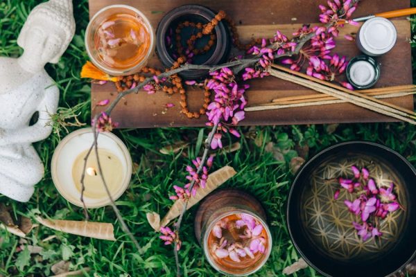 Peaceful outdoor meditation scene with Buddha, flowers, incense, and candles.